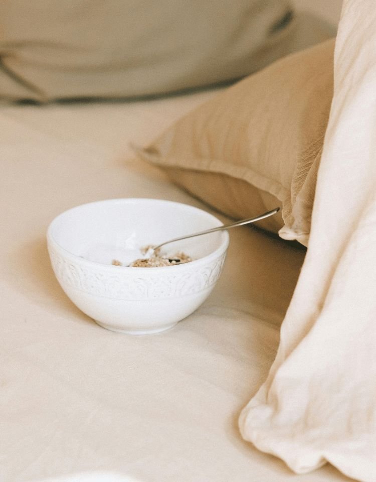 Witte kom met yoghurt en muesli op een beige bed, symbool voor zacht en mindful eetgedrag Witte kom met yoghurt en muesli op een beige bed, symbool voor zacht en mindful eetgedrag